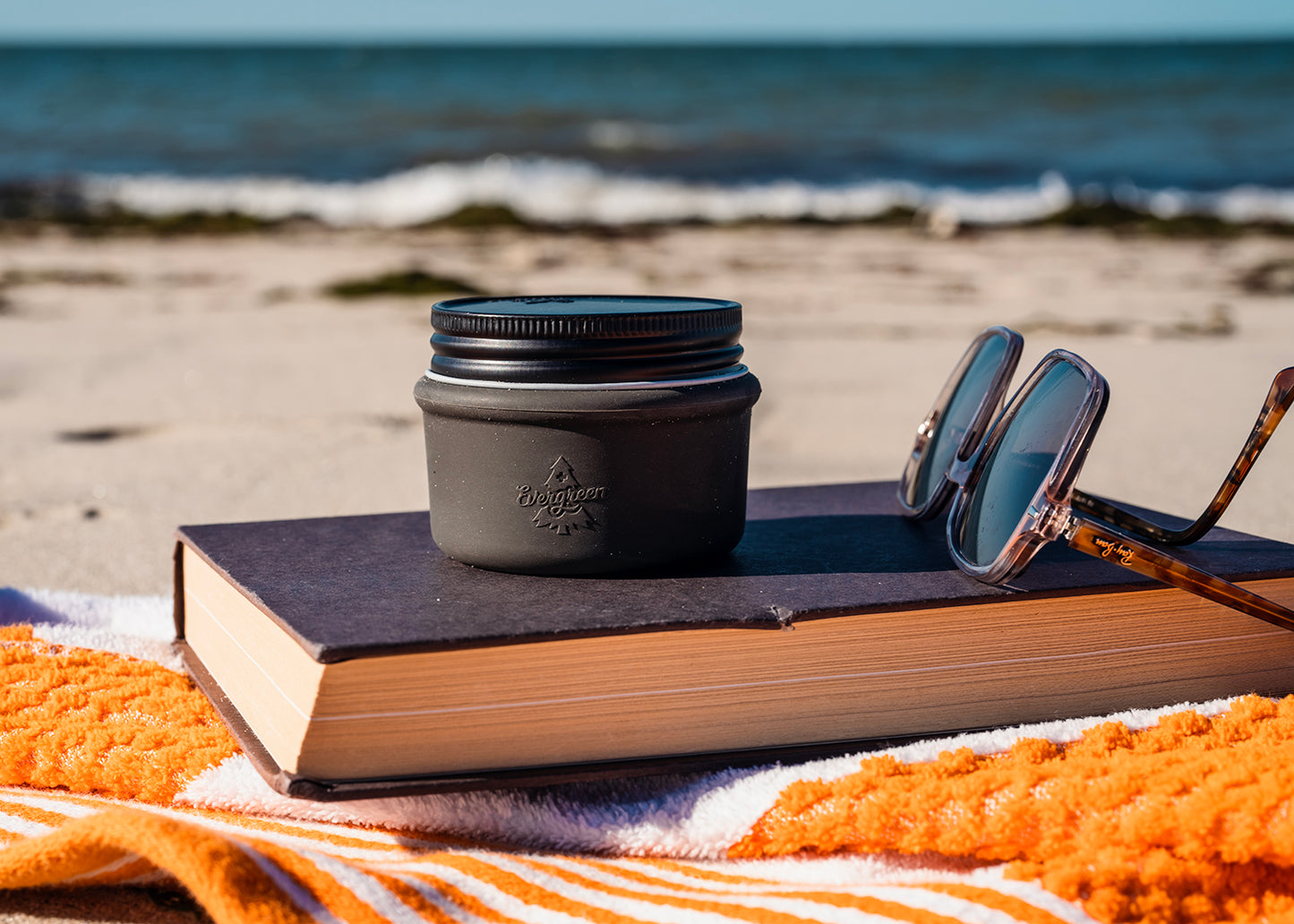 Evergreen Mini jar at the beach on top of a book